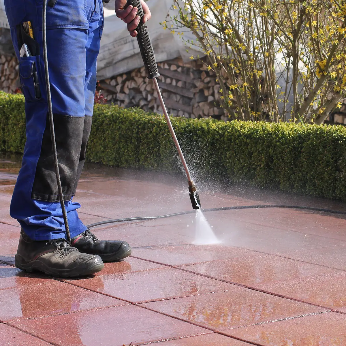 hausmeister am arbeiten draussen mit wasser am garten putzen